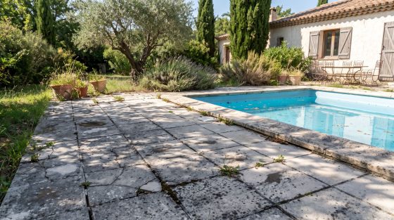 Plage de piscine en carrelage gris fissuré envahi d’herbes
